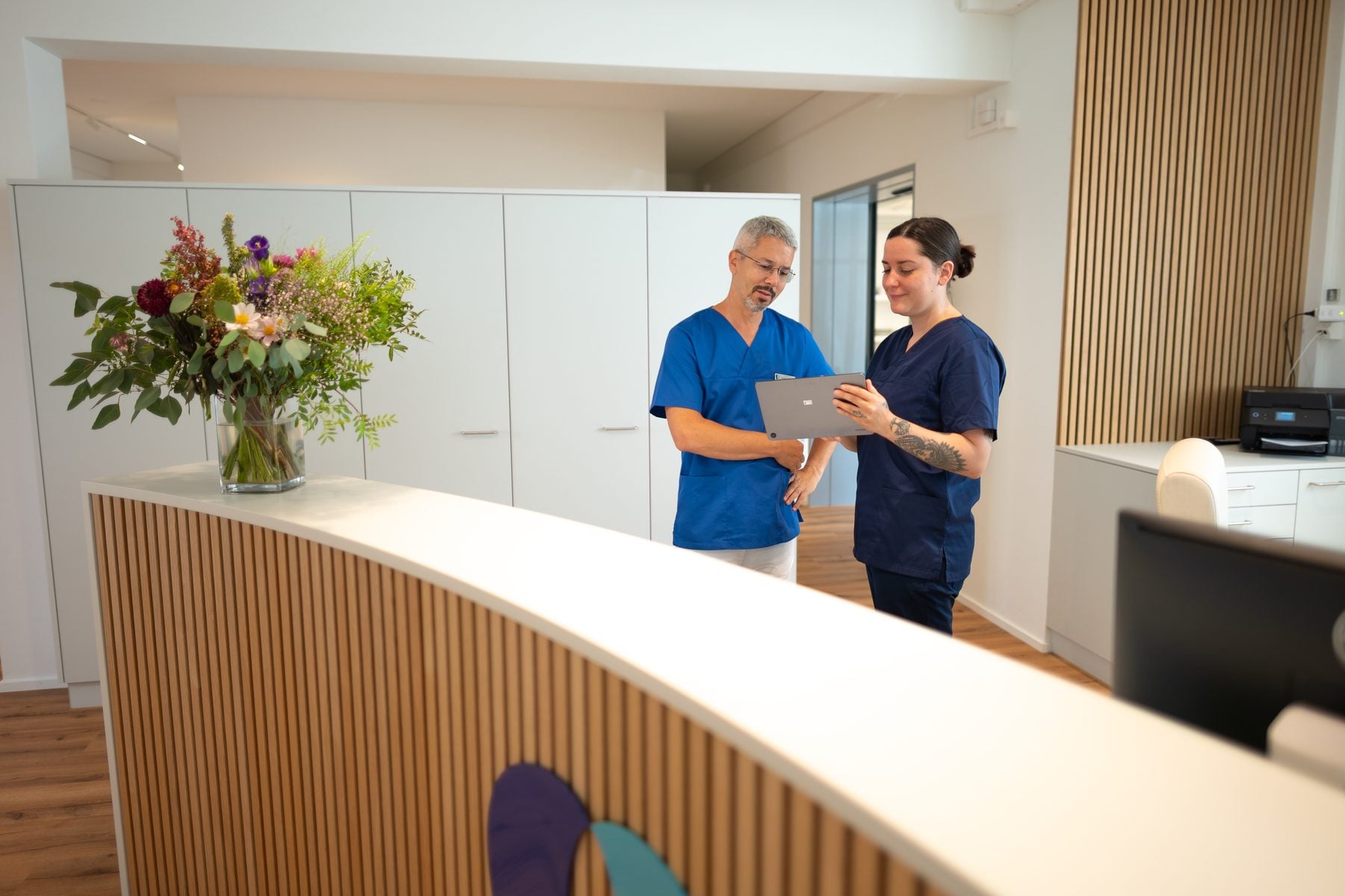 Empfang der Praxis mit Blumenstrauss, zwei Mitarbeitende besprechen sich am Tablet